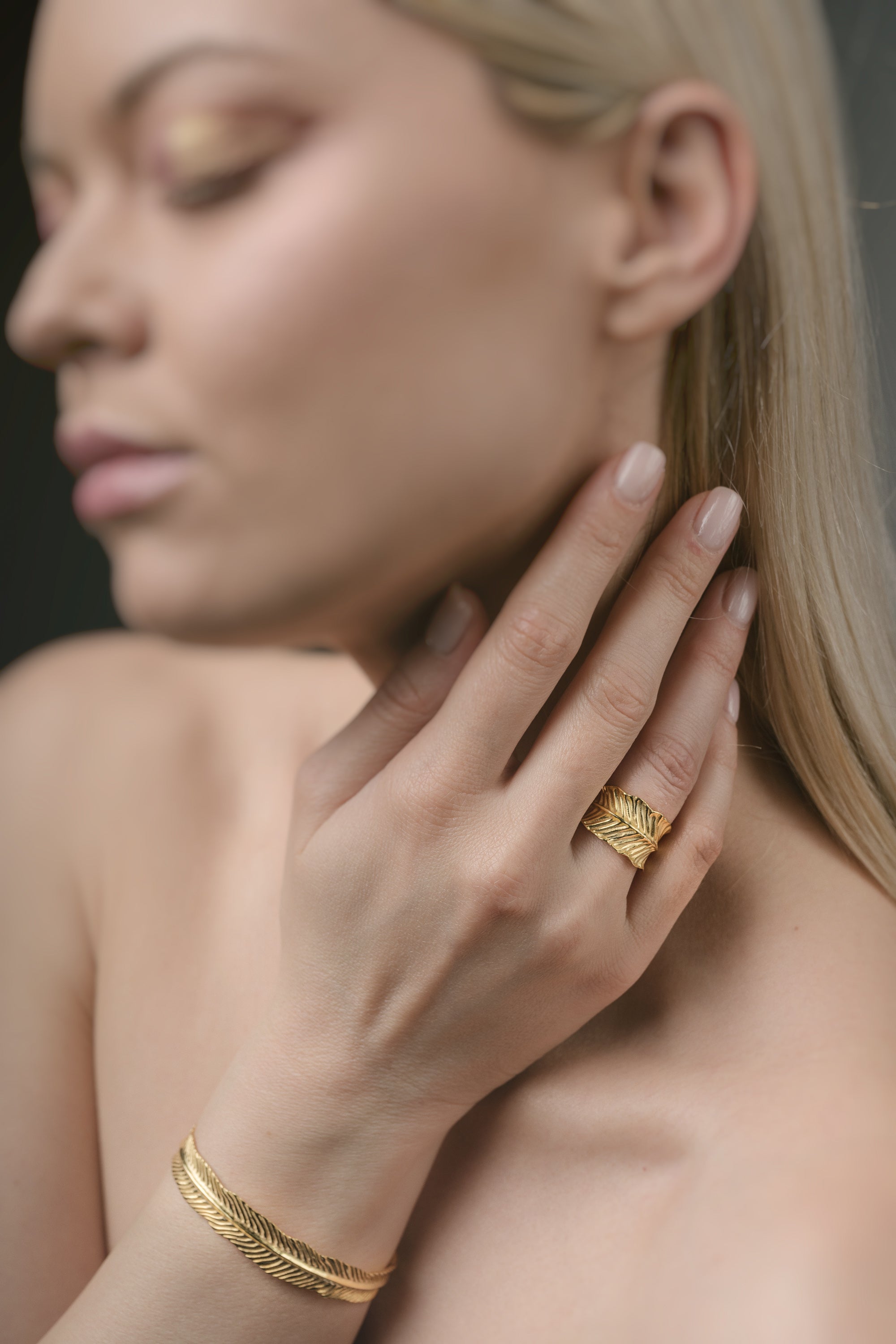 Woman wearing gold jewelry including a ring and bracelet against a neutral background