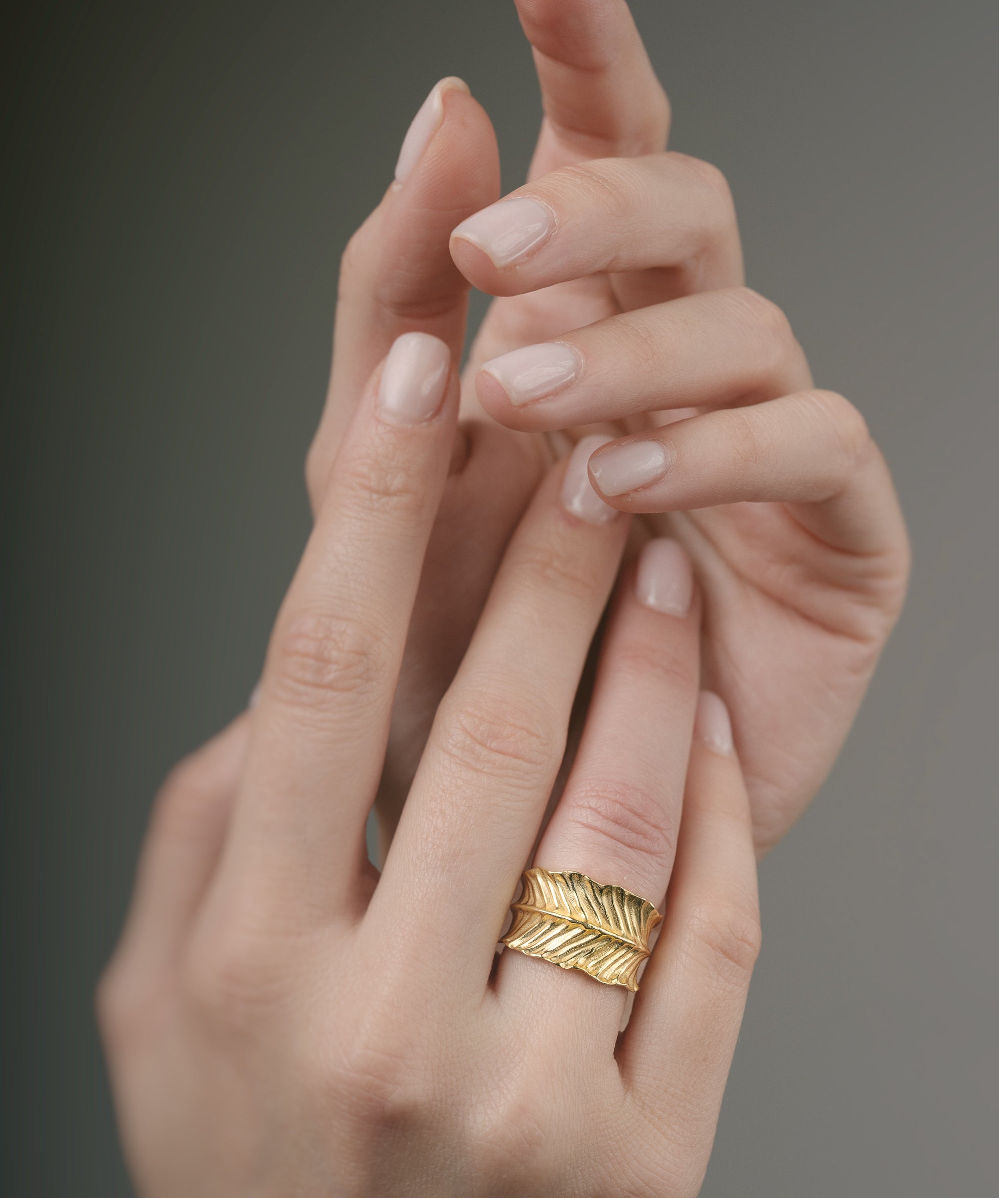 Gold ring on a finger against a neutral background