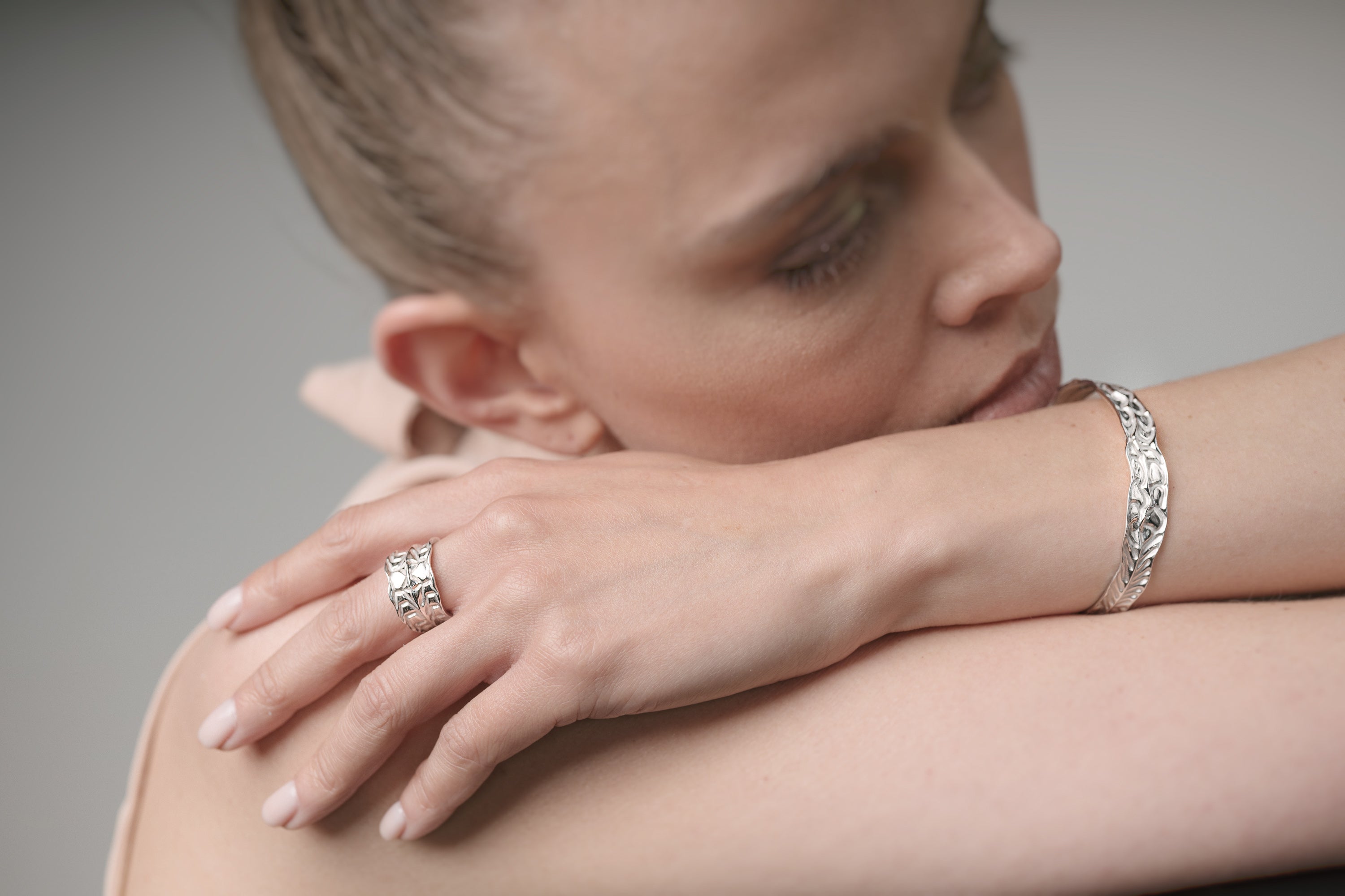 Close-up of a woman's hand with a ring and bracelet on a neutral background