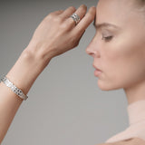Woman wearing a white gold bracelet and ring on a neutral background