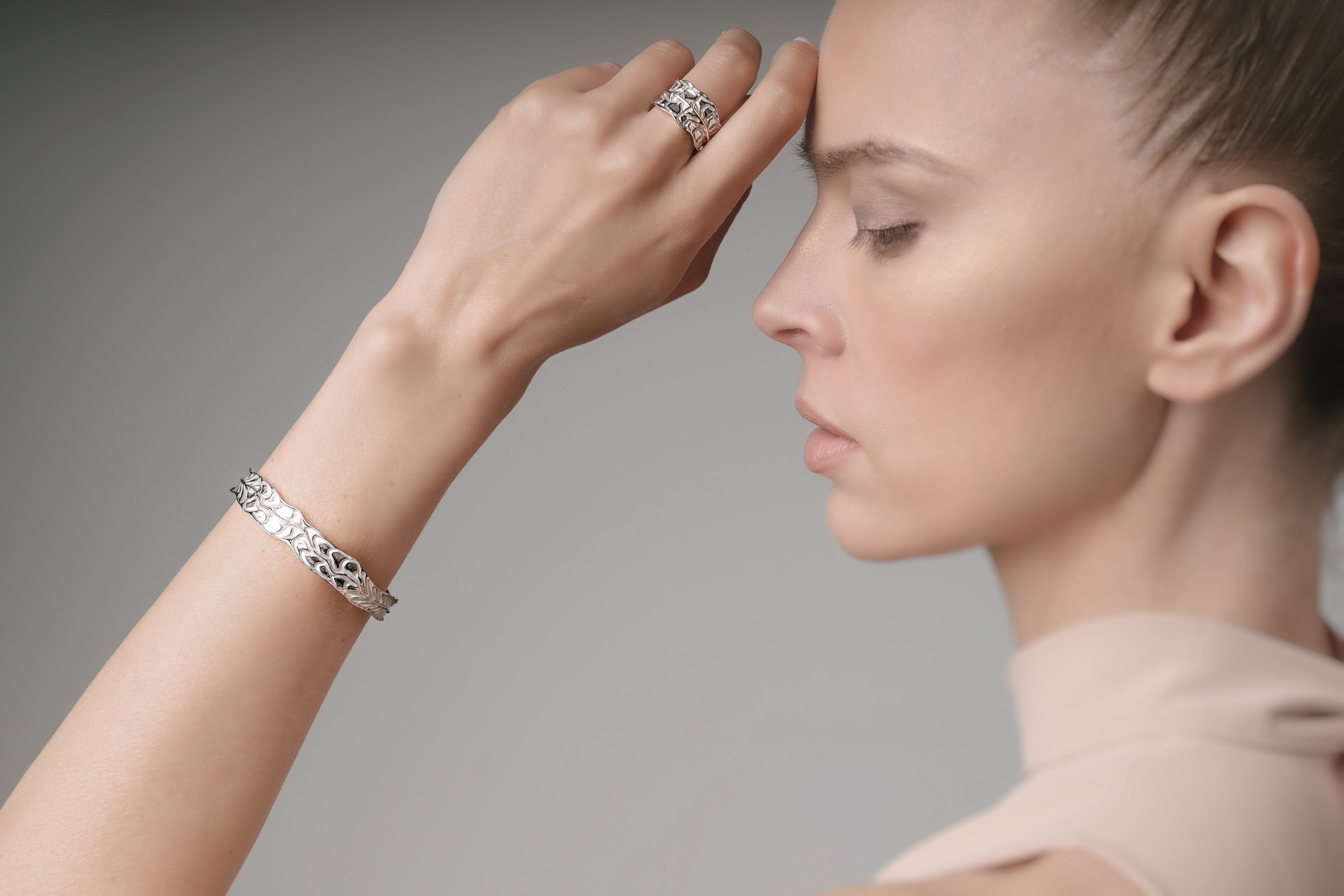 Woman wearing a white gold bracelet and ring on a neutral background