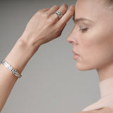 Woman wearing a silver bracelet and ring on a neutral background