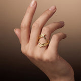 Hand wearing a gold ring with a leaf design on a brown background