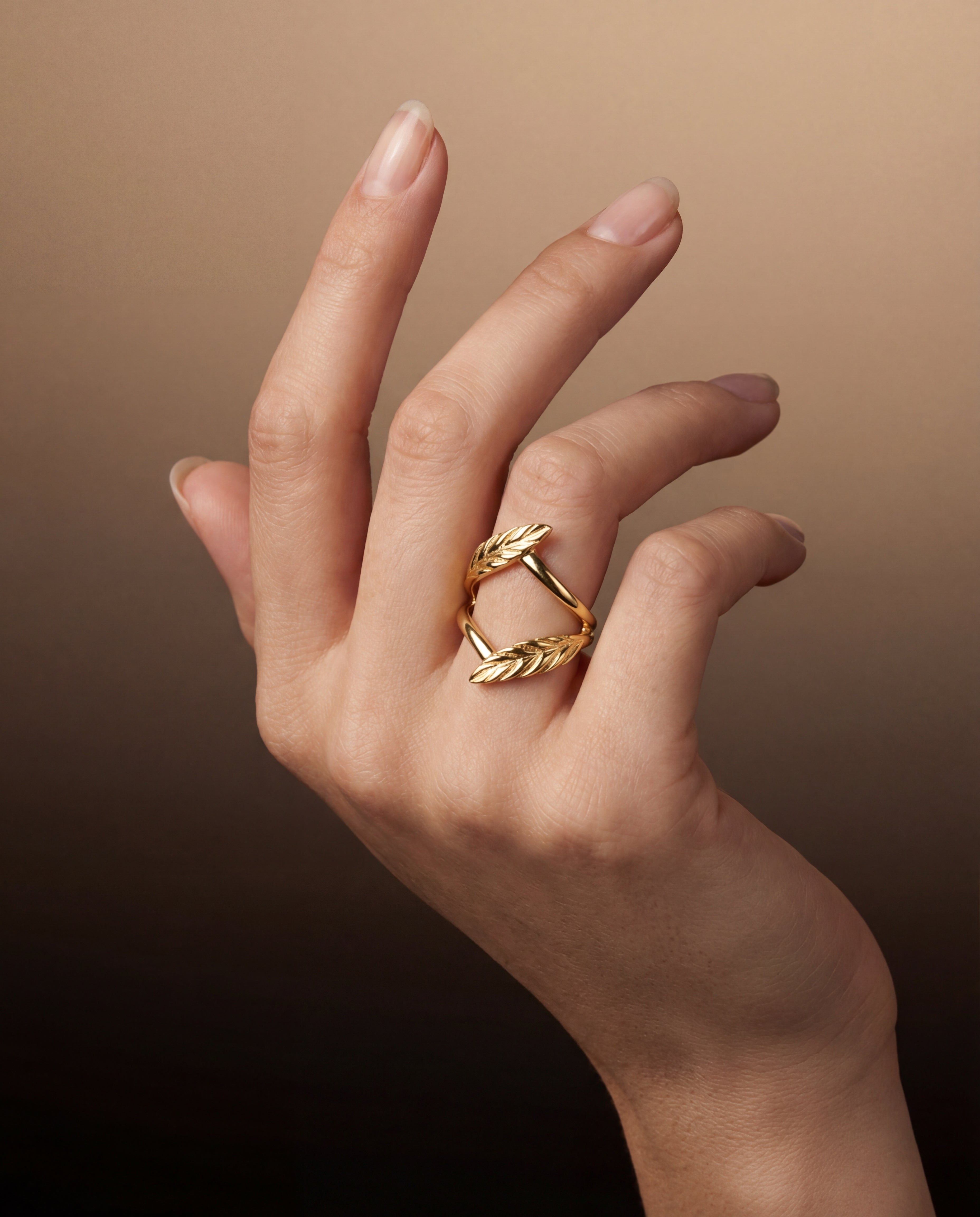 Hand wearing a gold ring with a leaf design on a brown background