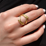 Gold ring with a double olive leaf design on a hand with a black background
