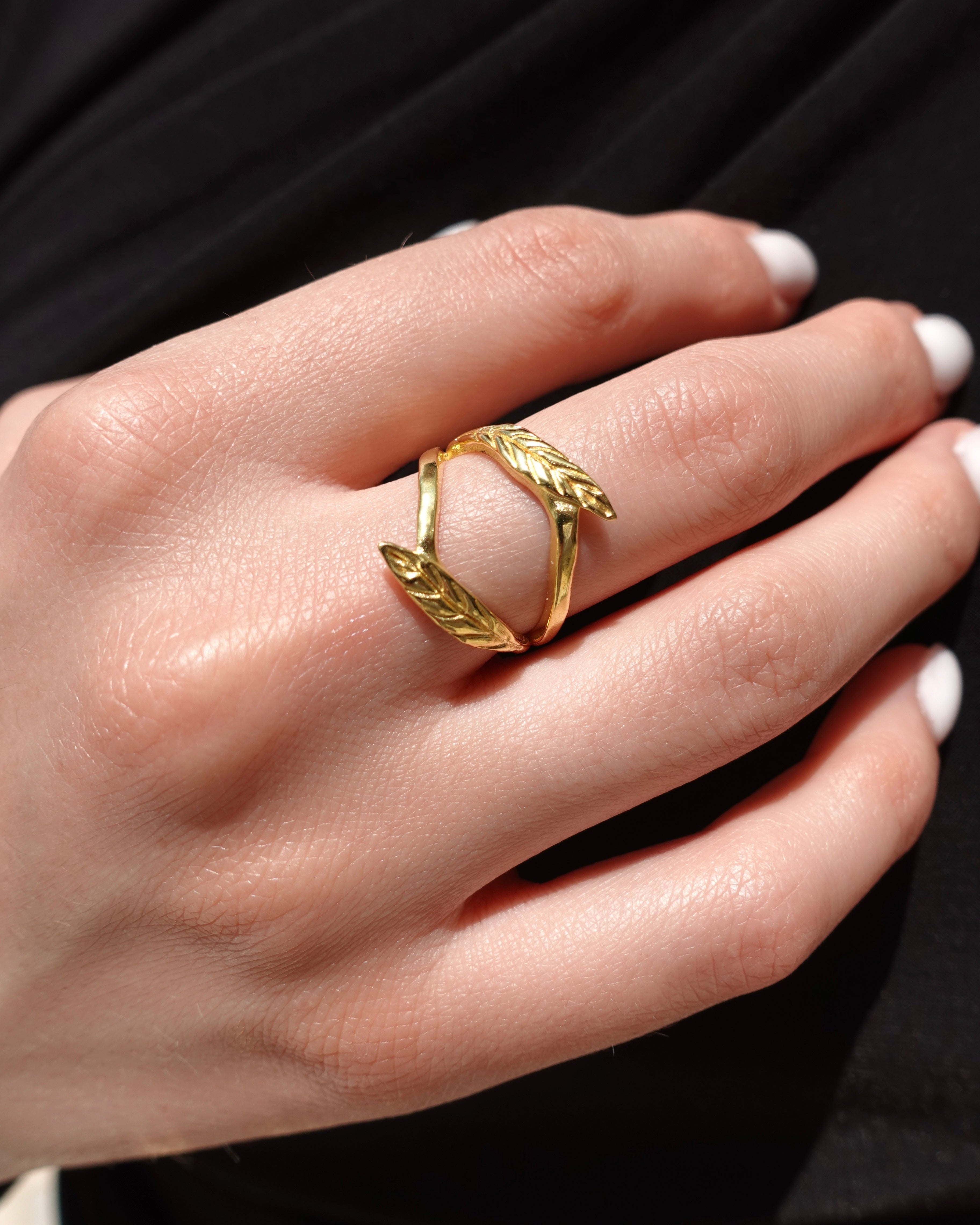 Gold ring with a double olive leaf design on a hand with a black background