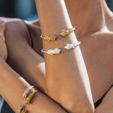 Close-up of a person wearing gold and silver bracelets with animal heads. 