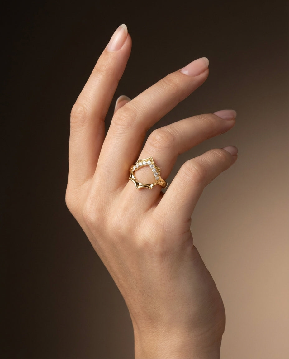 Hand wearing a gold ring with a heart design on a gradient background