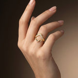 Hand wearing a gold ring with a heart design on a gradient background