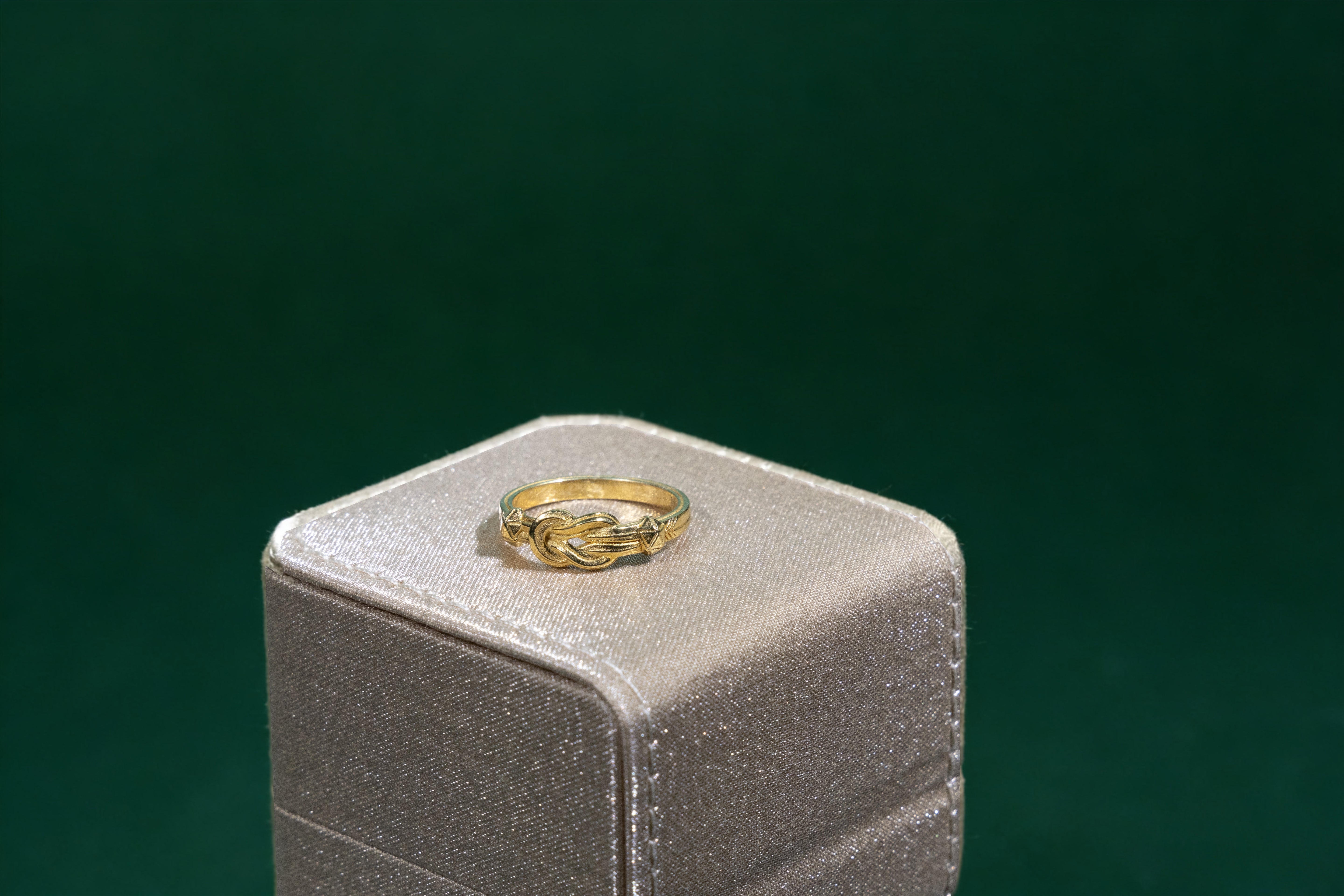 Gold Hercules knot ring on a gray jewelry box with a green background