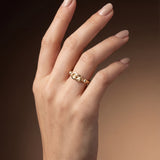 Hand wearing a gold Hercules knot ring on a gradient brown background