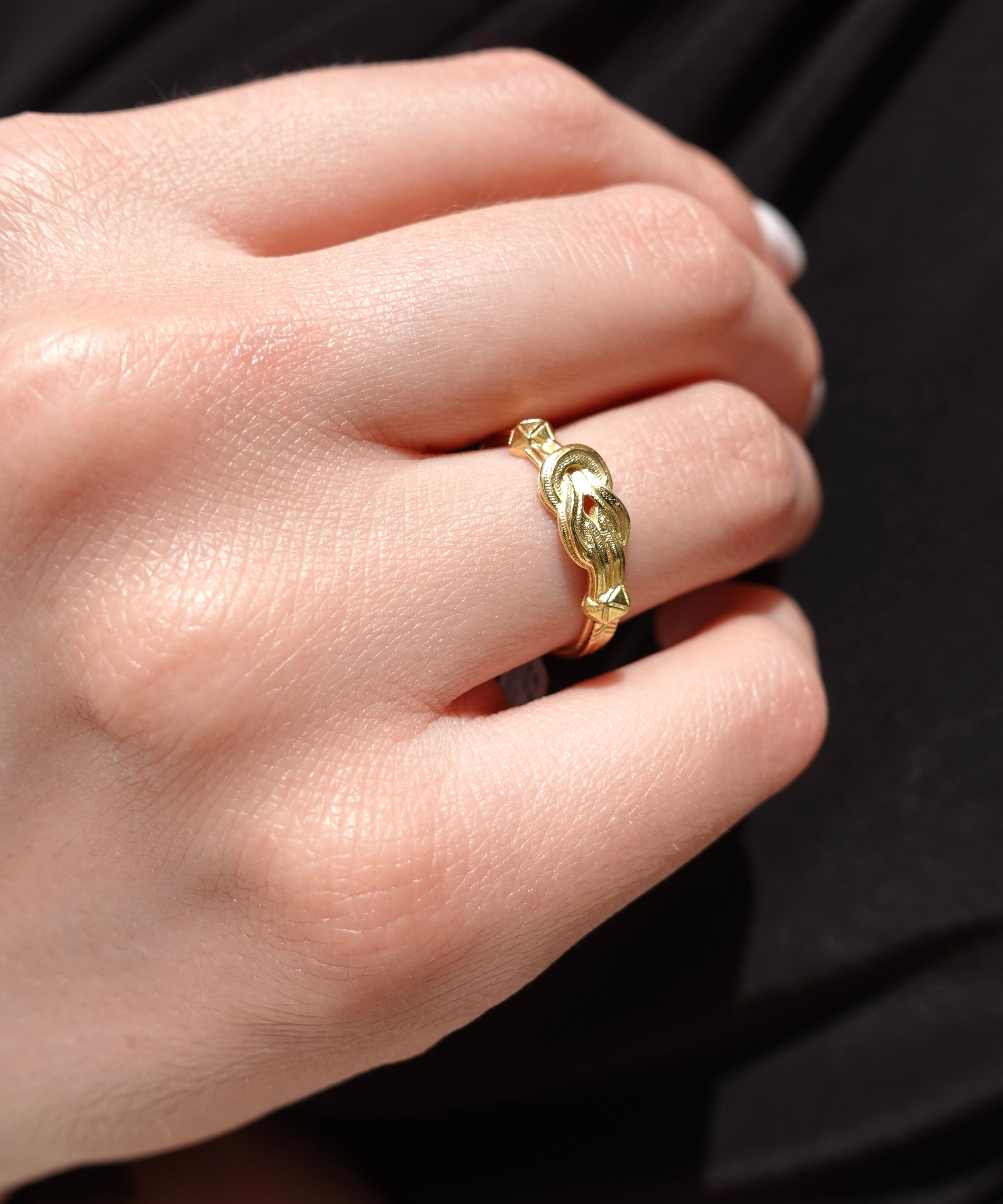 A model wearing a golden ring that has a hercules knot shape. 