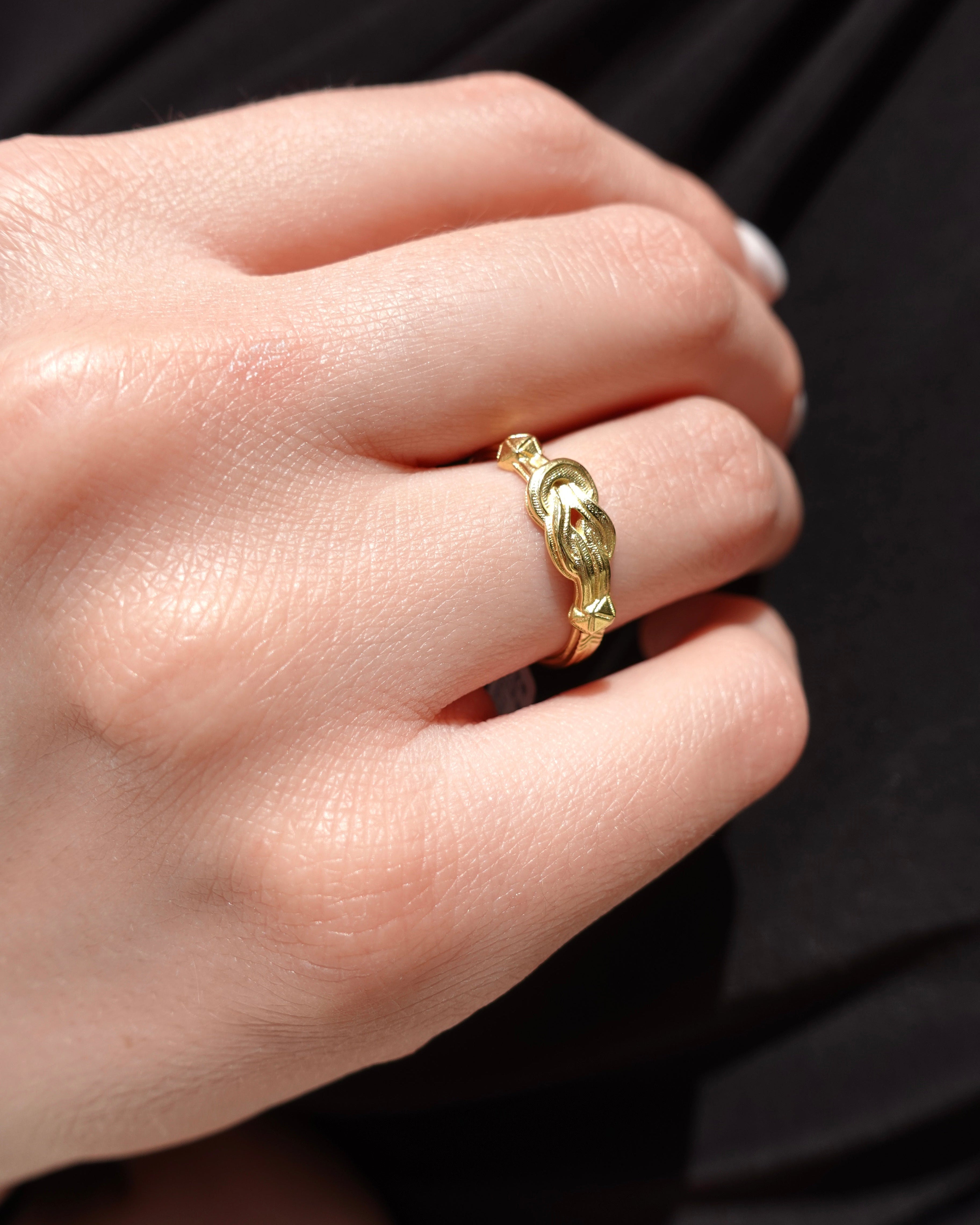 A model wearing a golden ring that has a hercules knot shape. 