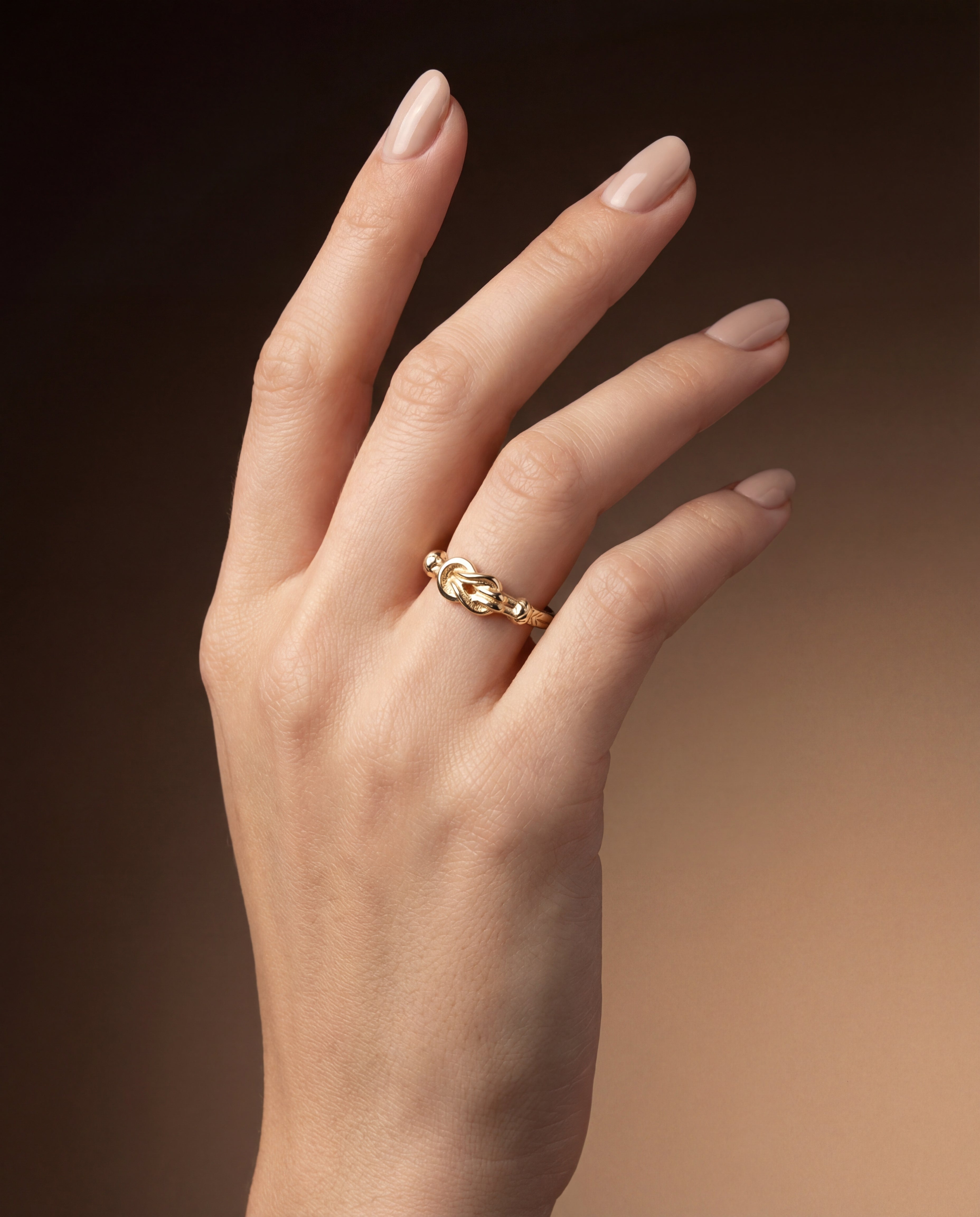 Hand wearing a gold Hercules knot ring on a gradient brown background