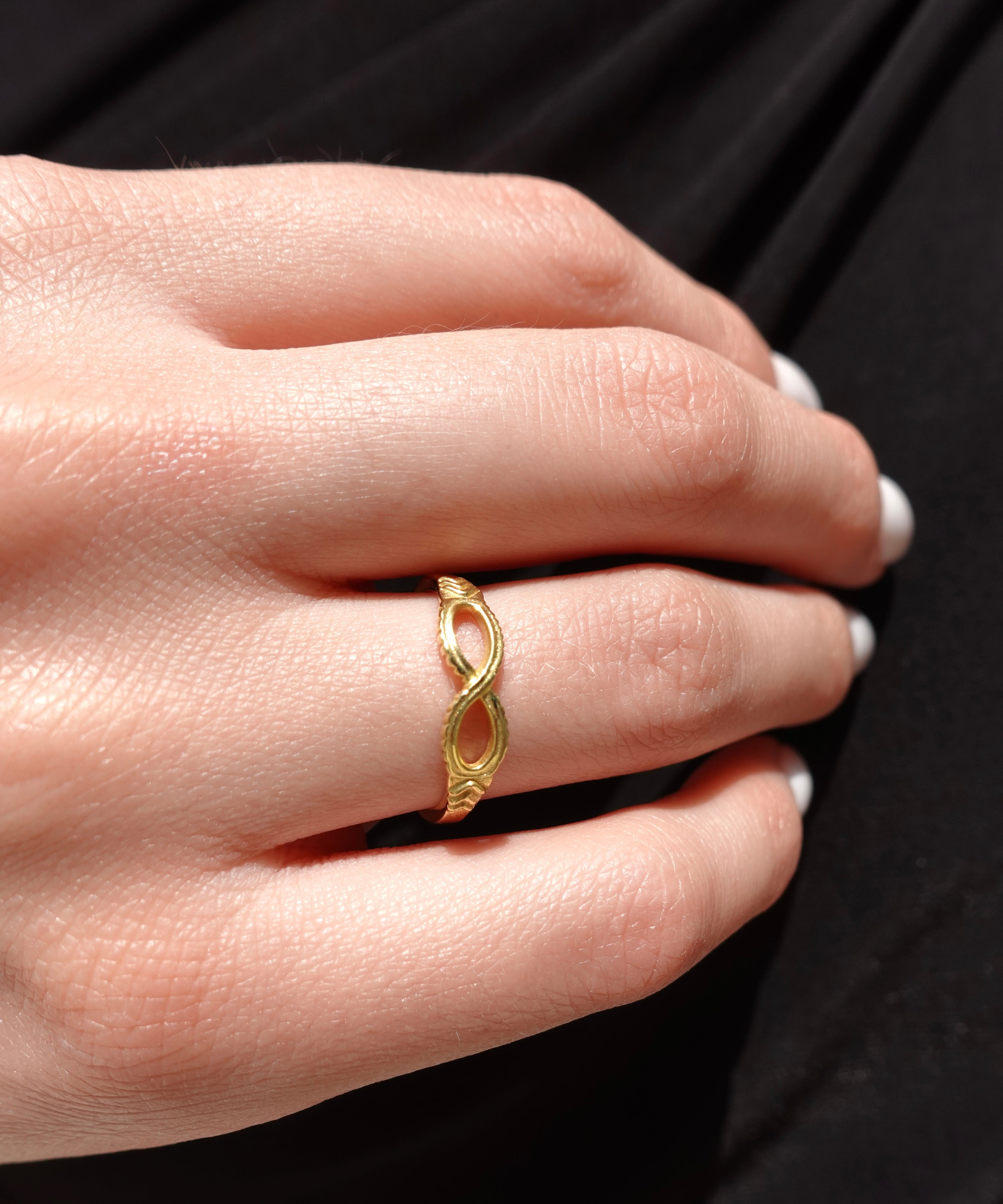 Gold ring with infinity shape on a person's finger against a black background