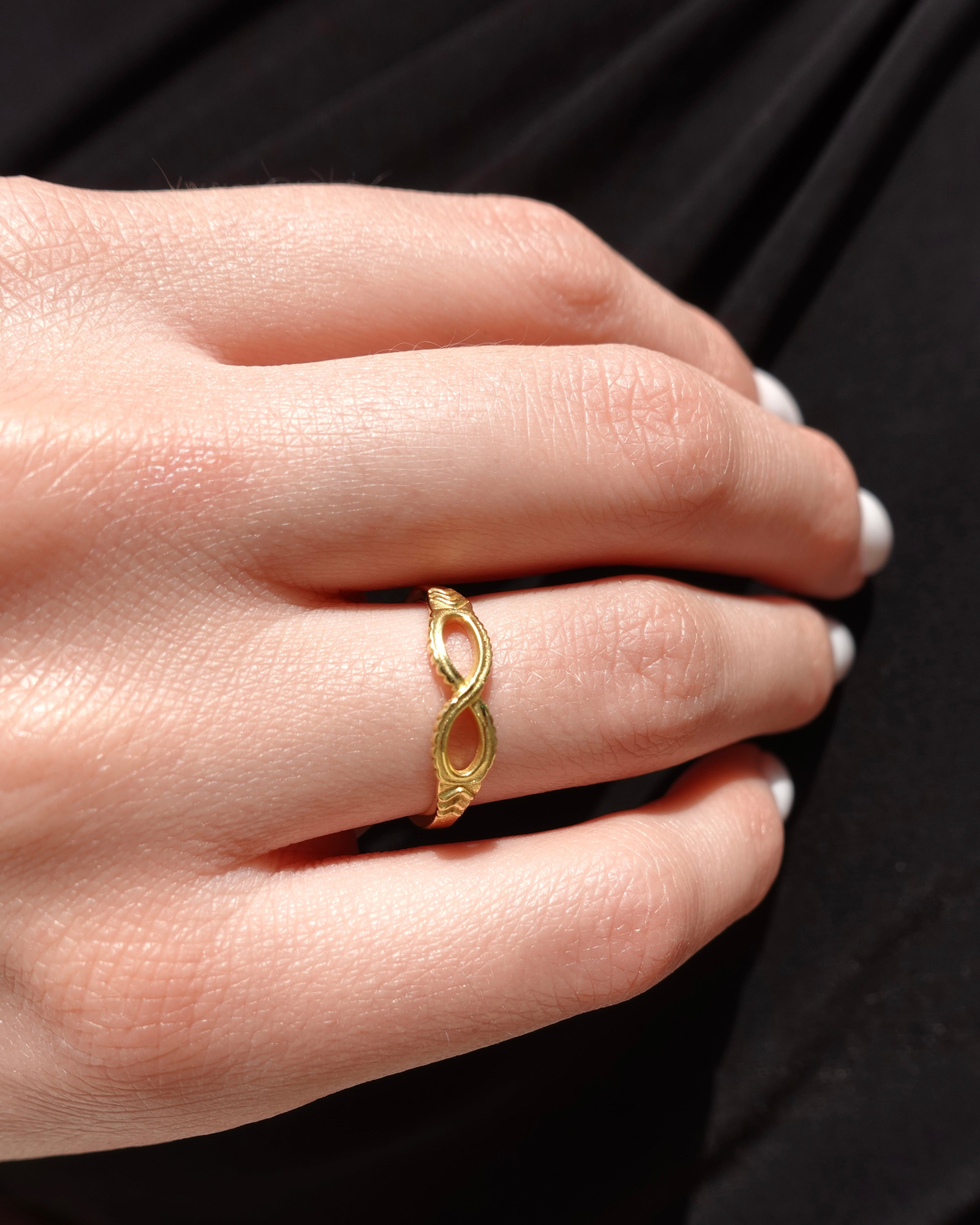 Gold ring with infinity shape on a person's finger against a black background