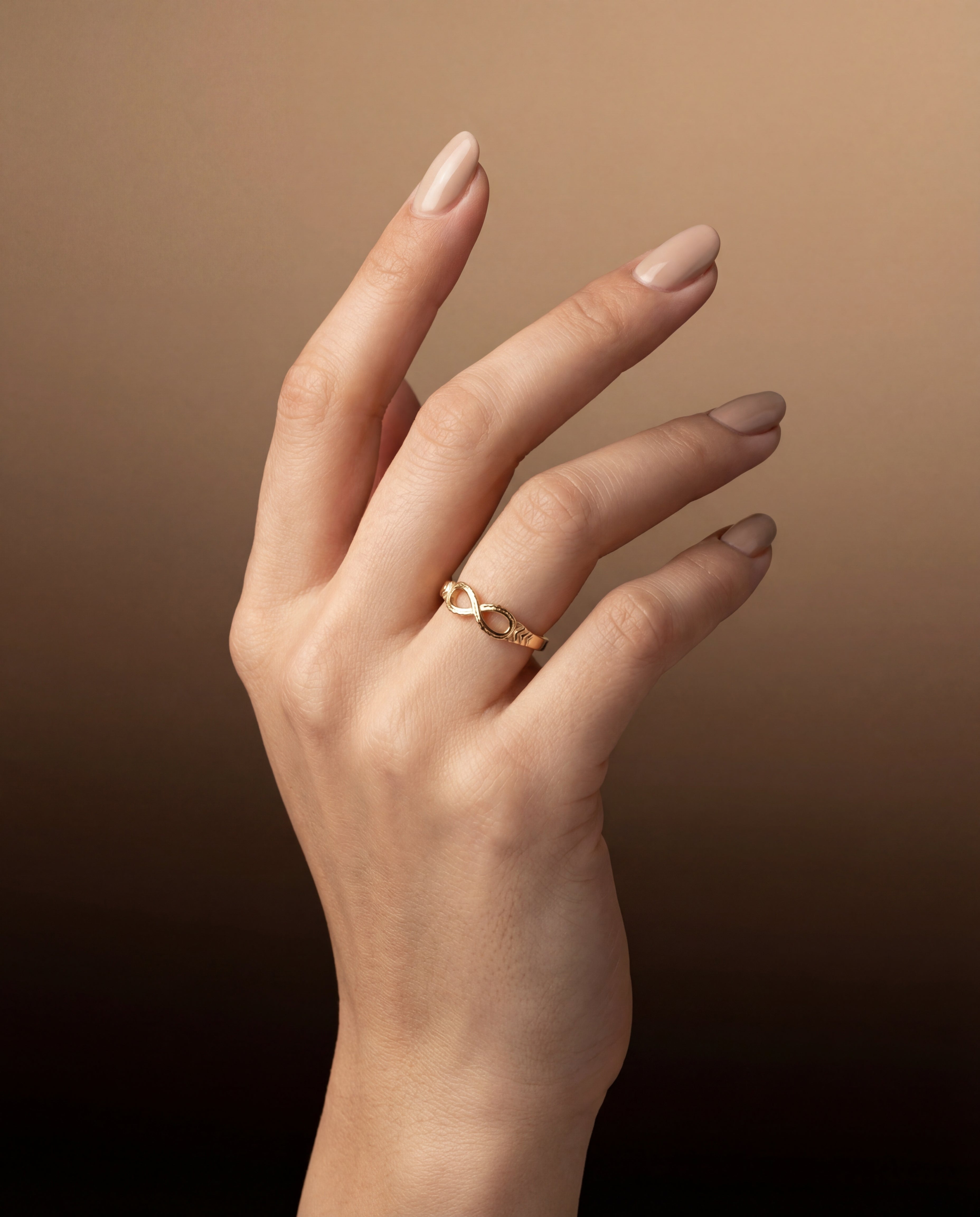 Hand wearing a gold infinity ring on a brown background