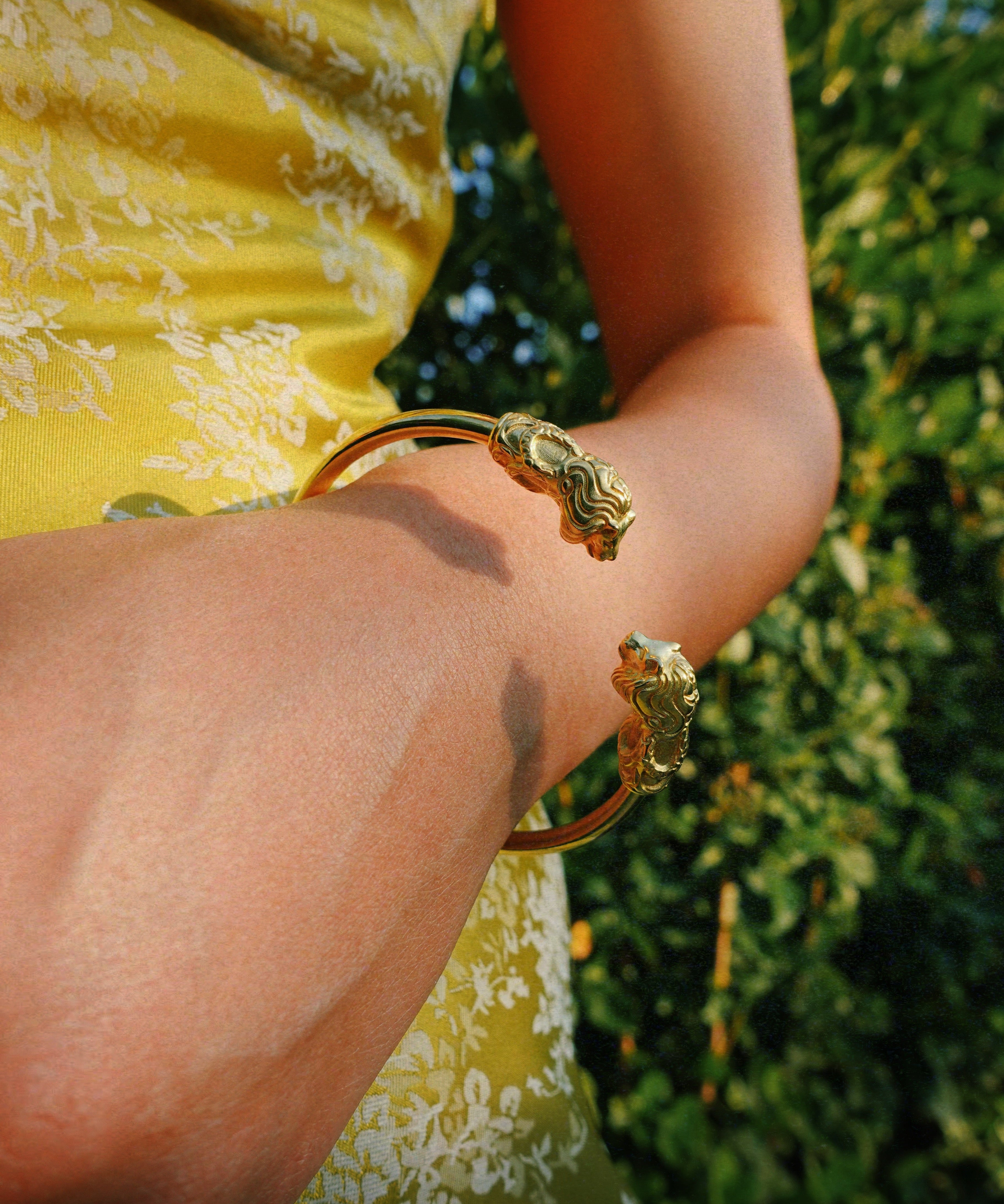 a person wearing lion-head bracelet with leafy background 