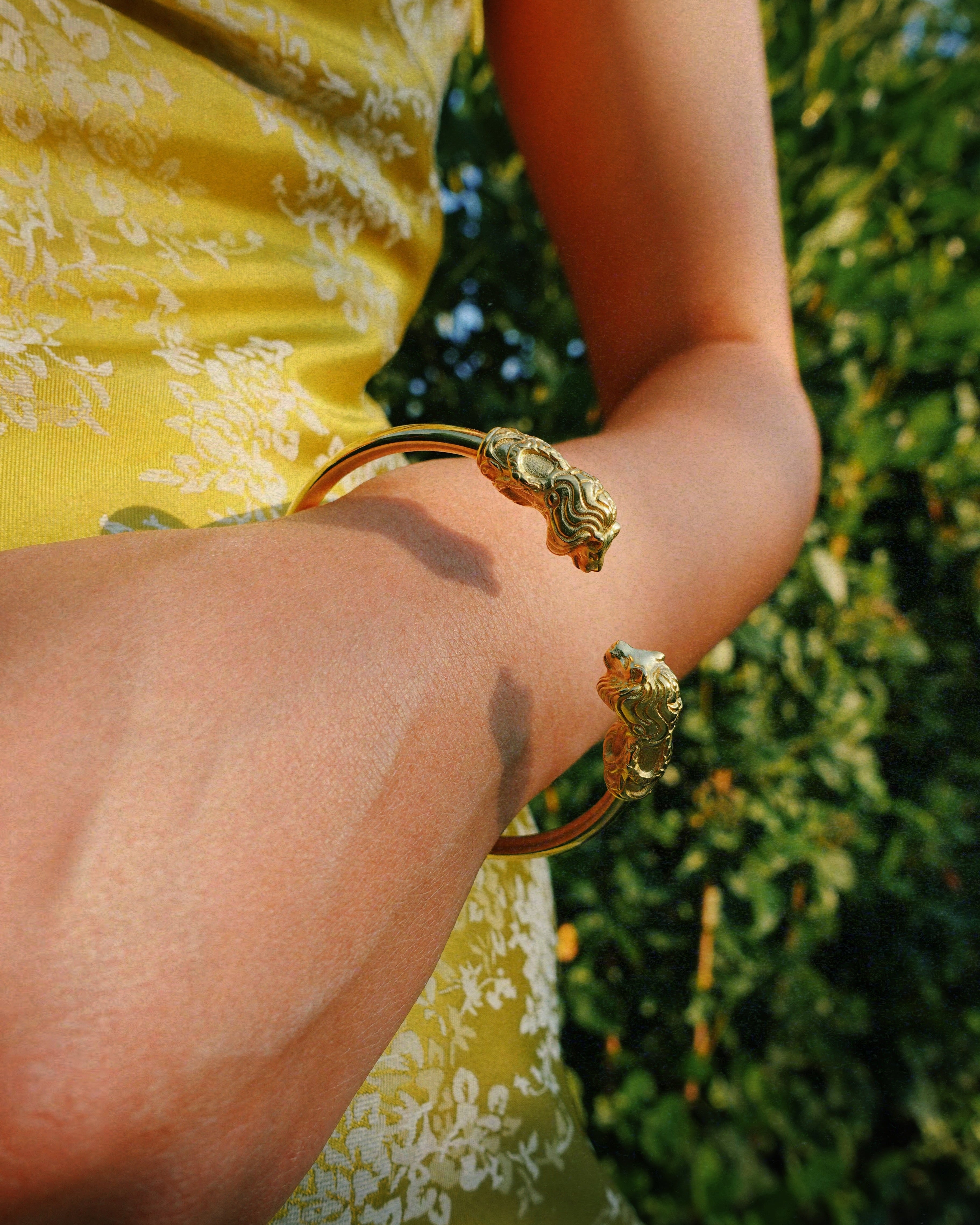 a person wearing lion-head bracelet with leafy background 