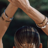 Person with hands raised wearing multiple bracelets against a blurred natural background