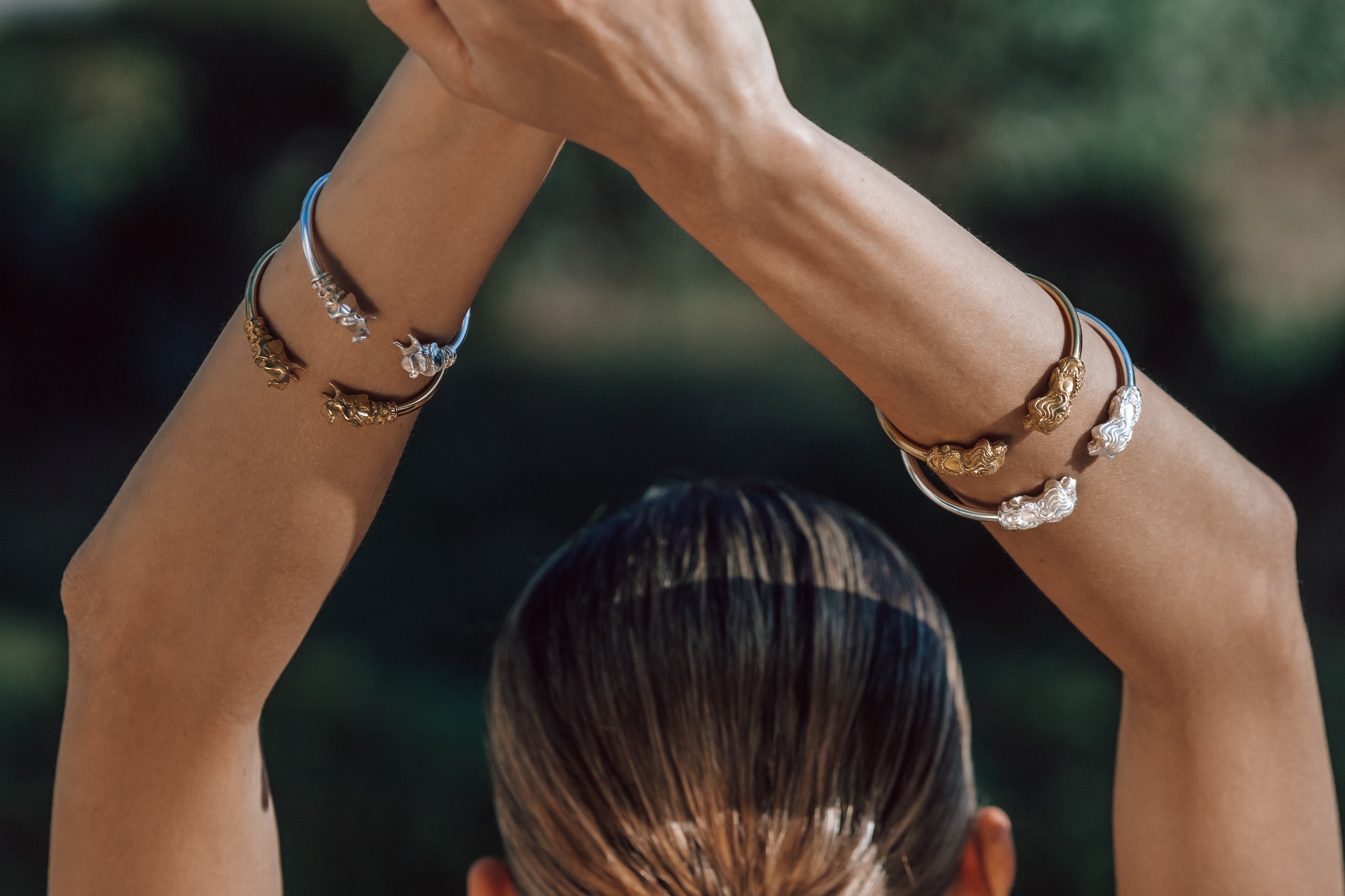 Person with hands raised wearing multiple bracelets against a blurred natural background