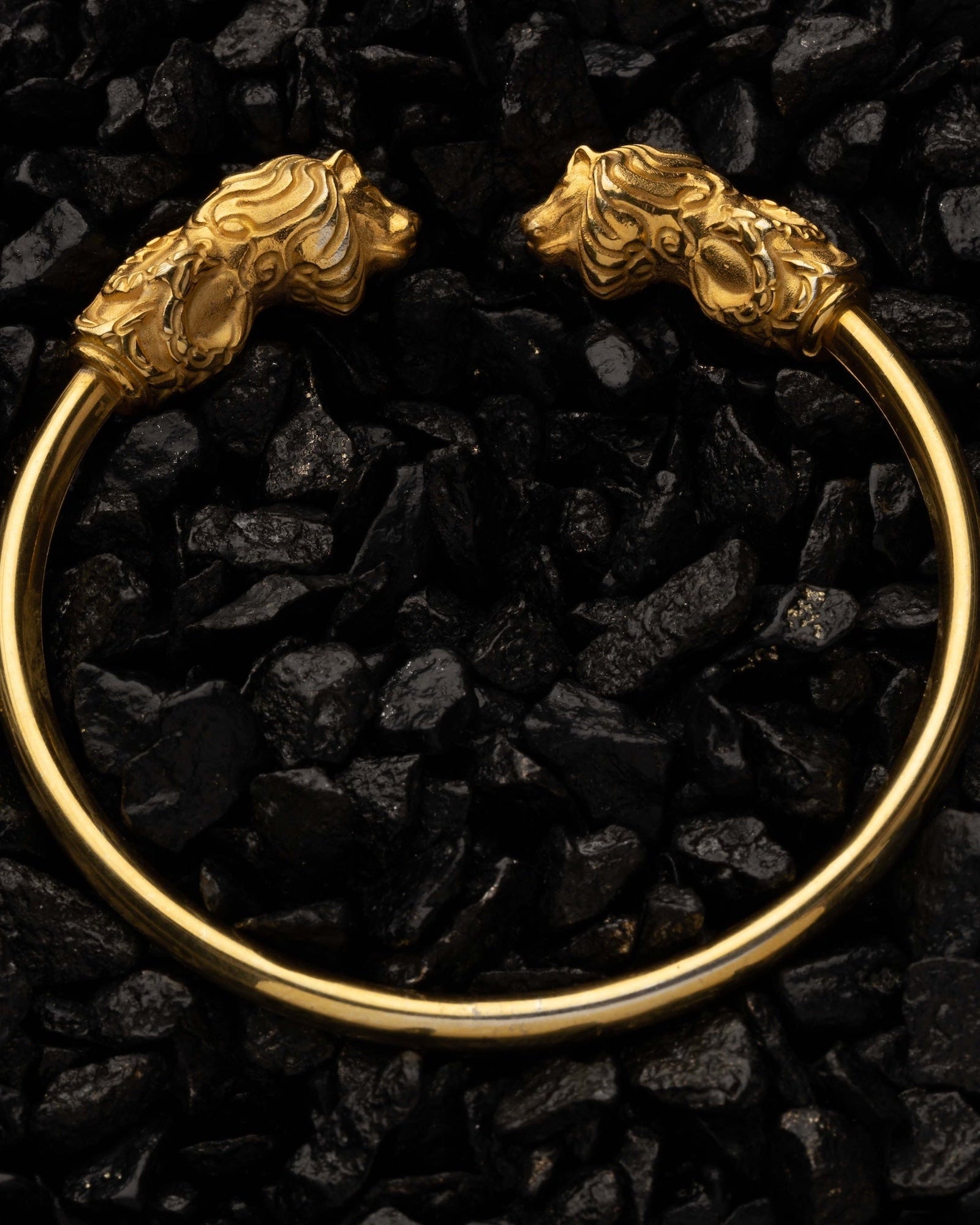 Gold bracelet with lion head designs on a black stone background