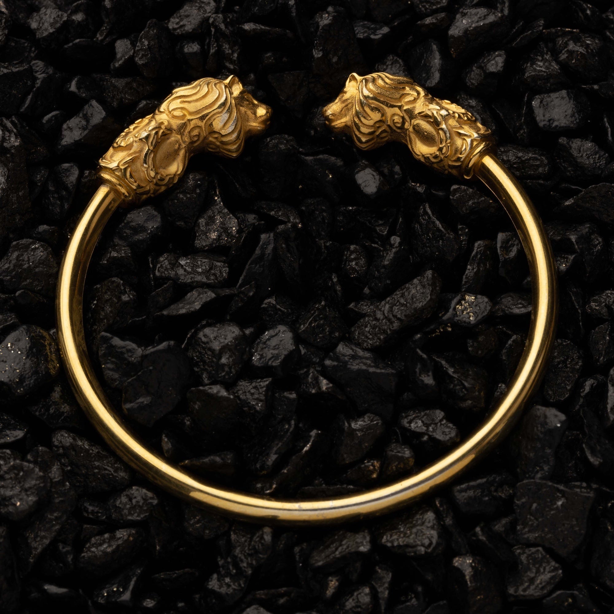 Gold bracelet with lion head designs on a black stone background