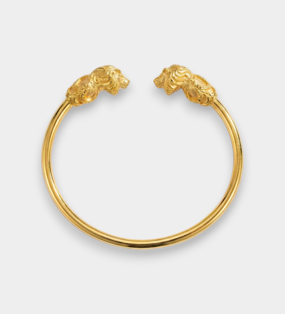 Gold bracelet with lion head clasps on a light gray background