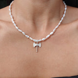 A close-up of a person's neck and upper chest wearing a silver necklace with irregular white pearl-like beads and a small axe pendant at the center.
