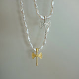 A double-strand necklace featuring white shell beads and two axe pendants, one in textured gold and one in silver with small clear stones, displayed against a plain light gray background.