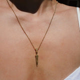 Gold necklace with a sword-shaped pendant on a person wearing a white top.