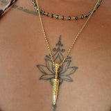 Gold necklace with a dagger pendant on a person's neck with visible tattoos.