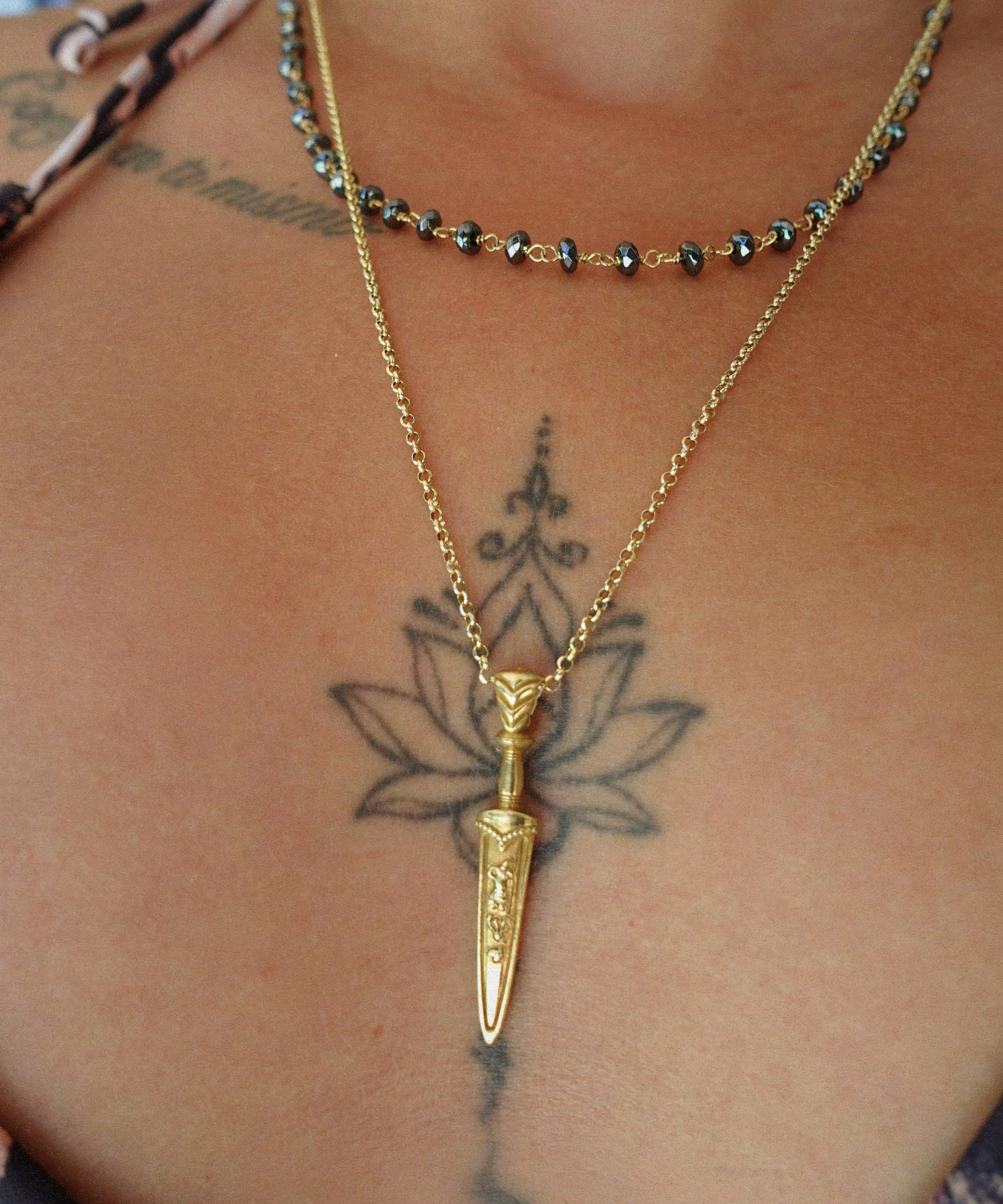 Gold necklace with a dagger pendant on a person's neck with visible tattoos.