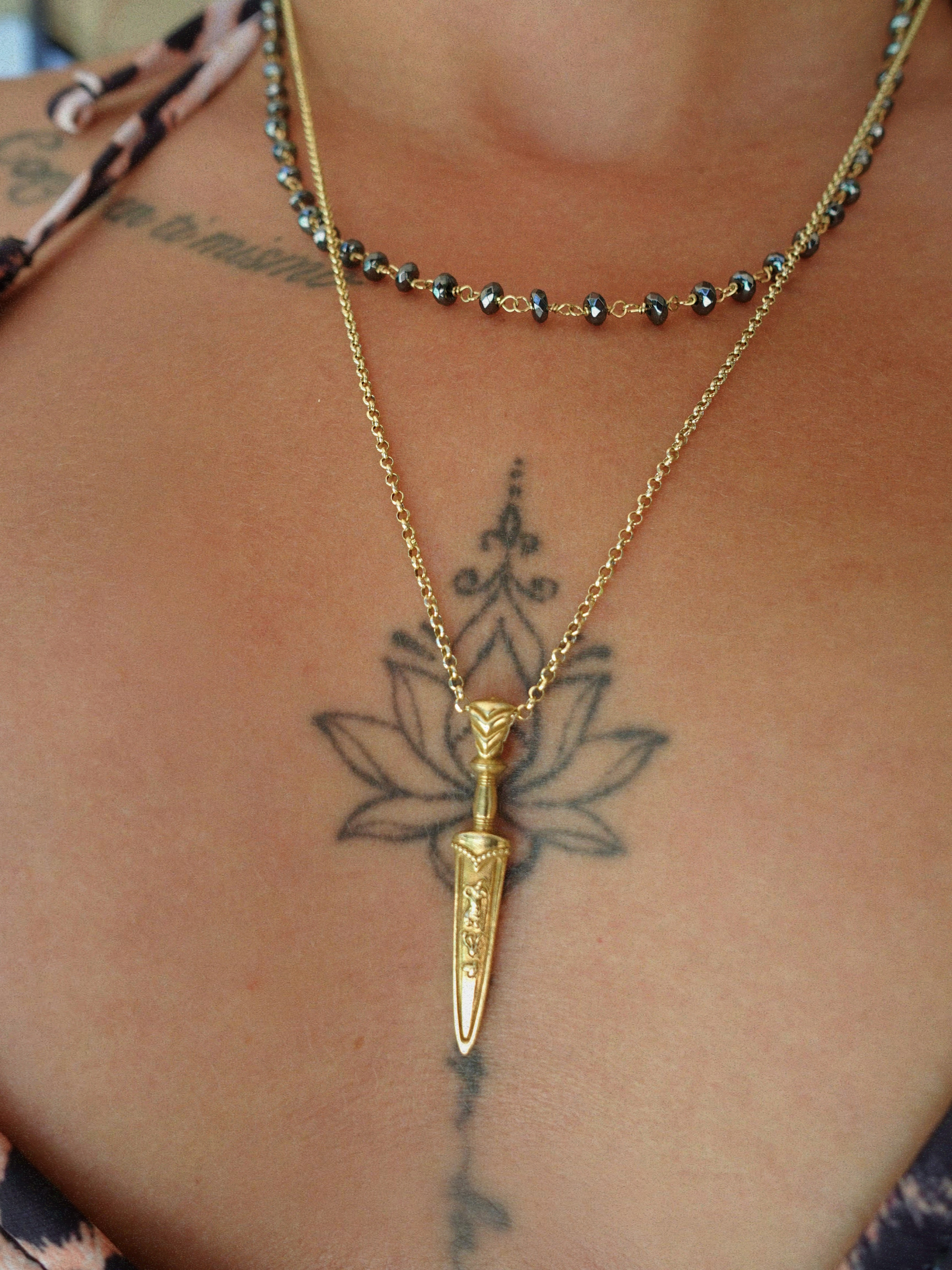 Gold necklace with a dagger pendant on a person's neck with visible tattoos.