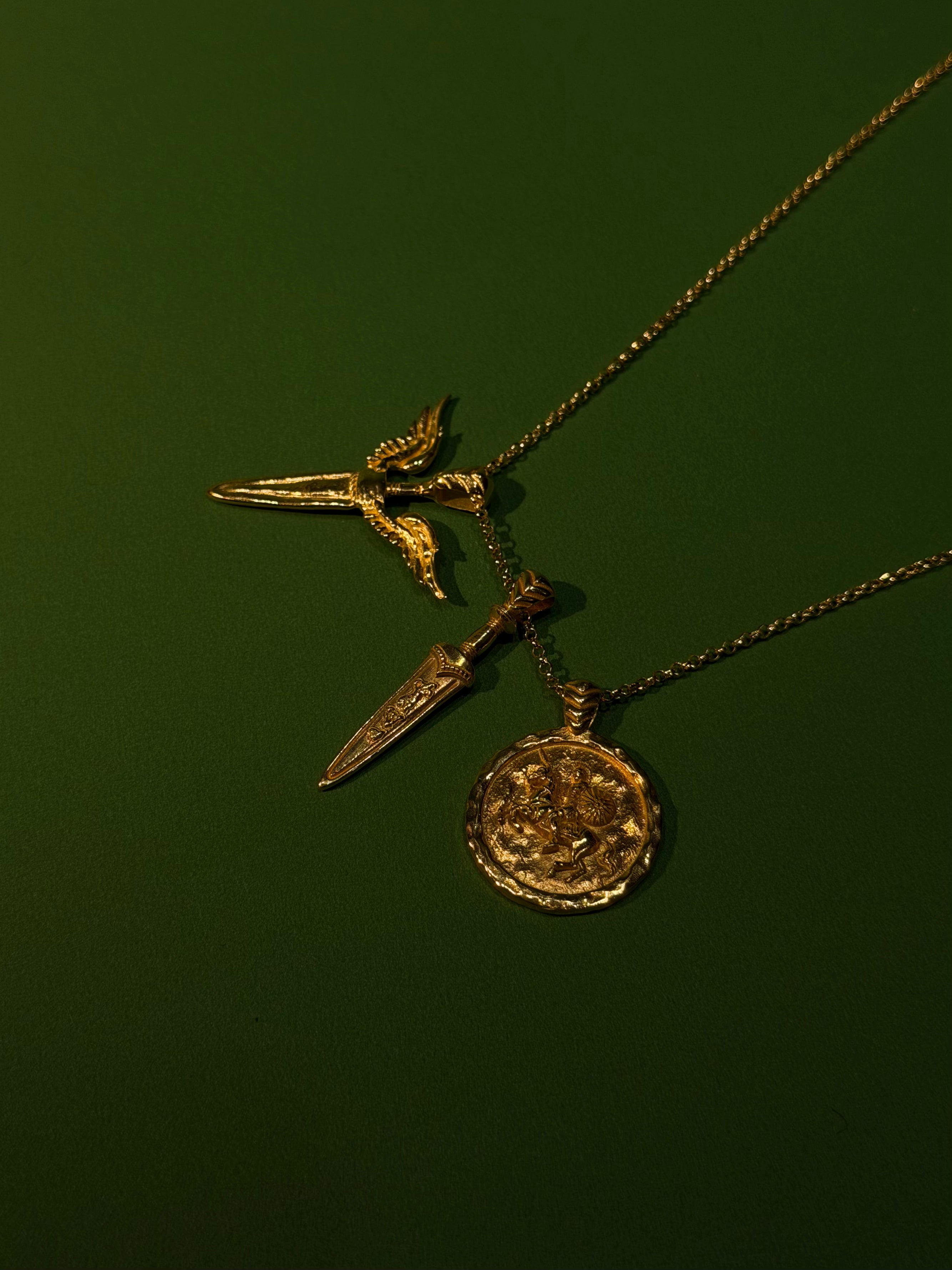 Gold necklace with three pendants on a dark green background