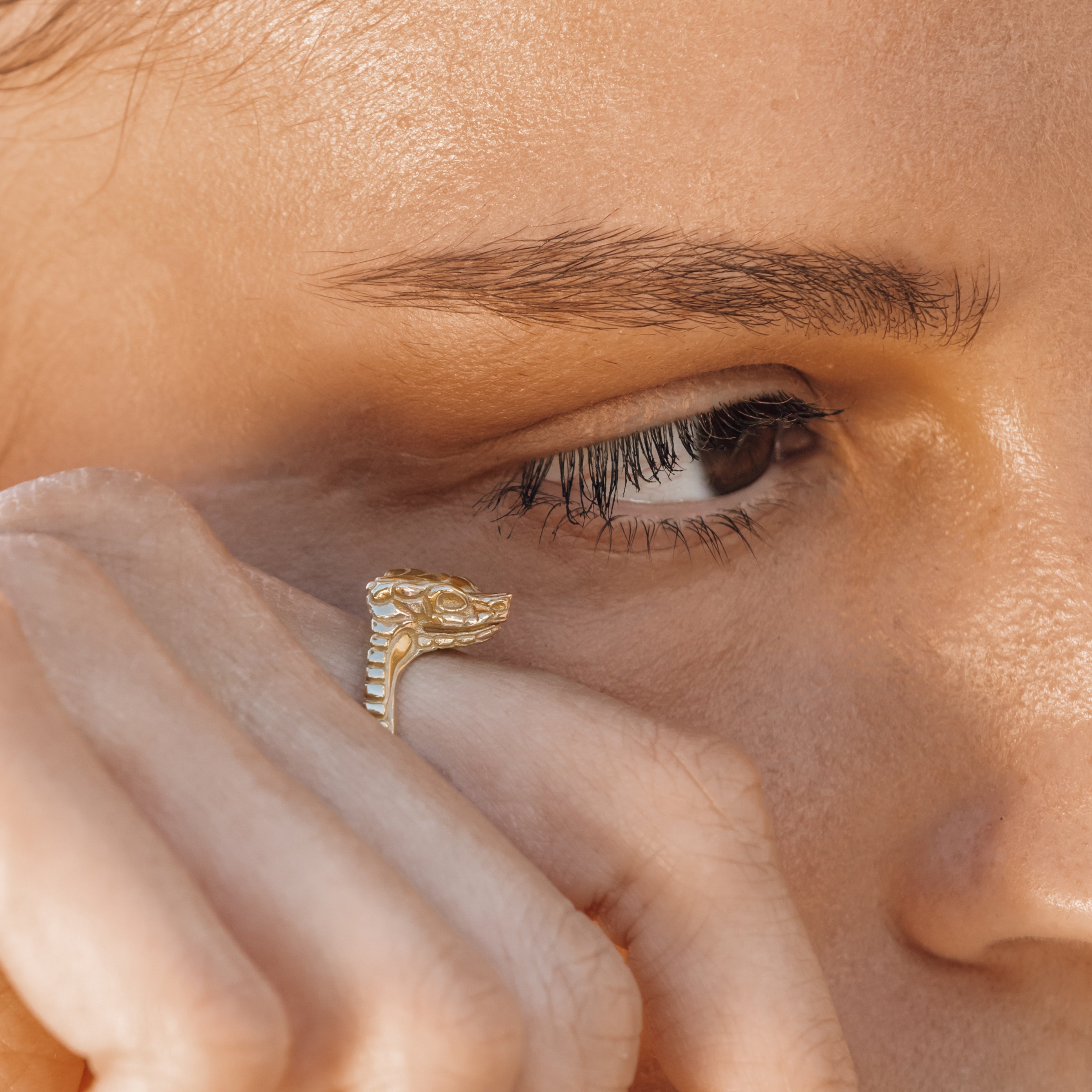 Close-up of a person wearing a gold snake ring on their finger.