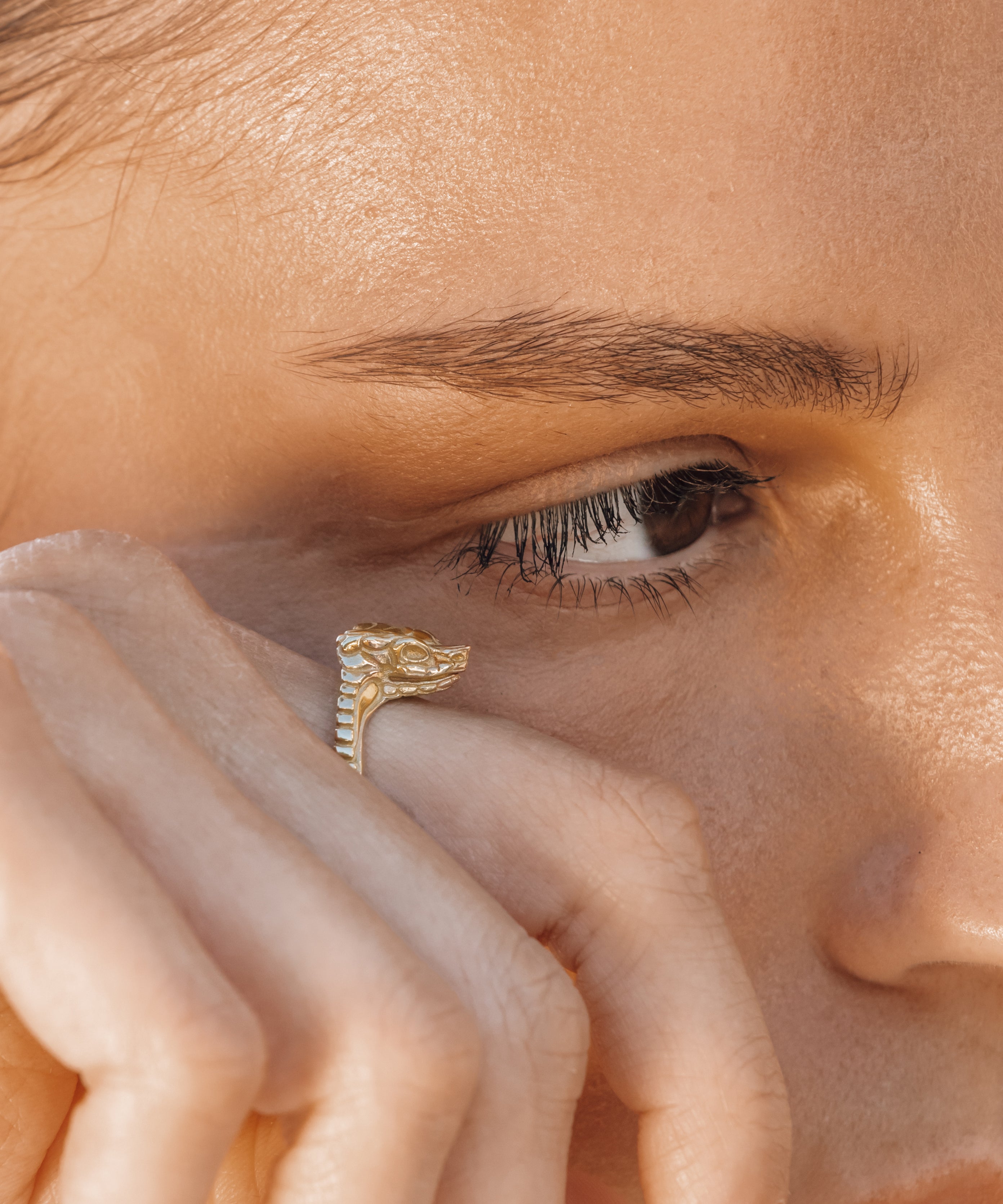 Close-up of a person wearing a gold snake ring on their finger.