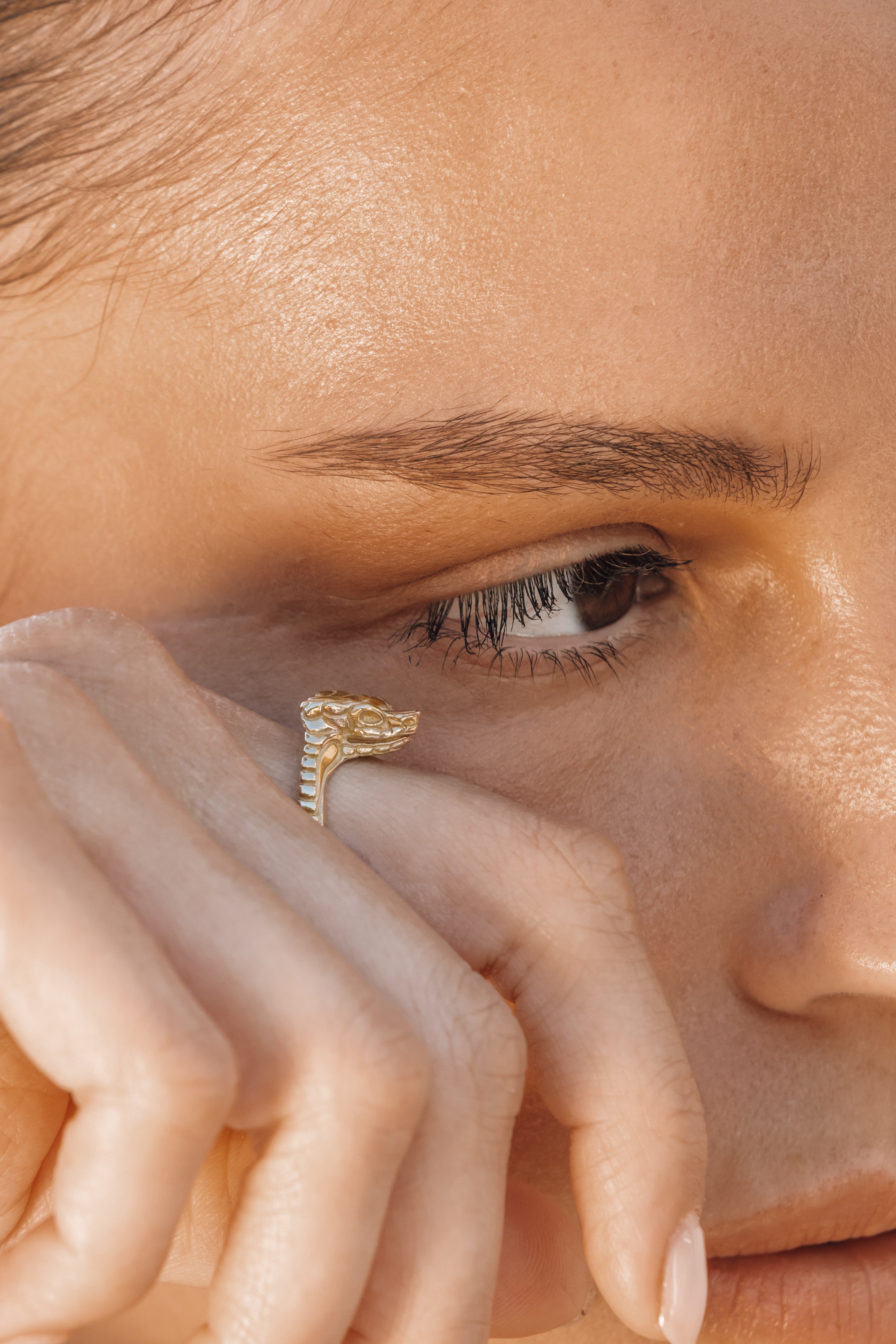 Close-up of a person wearing a gold snake ring on their finger.