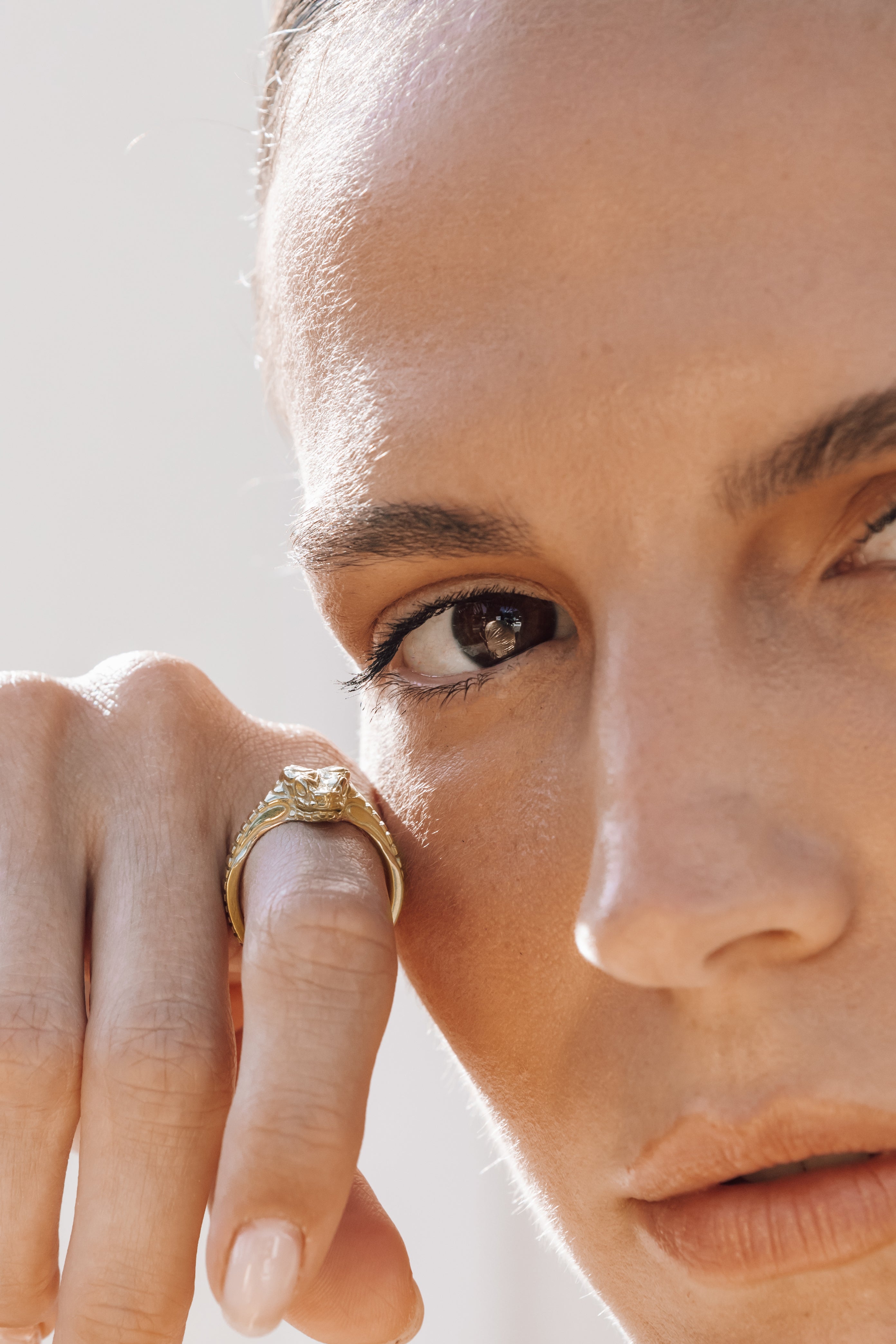 Close-up of a person wearing a gold snake ring on a light background