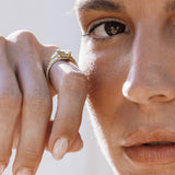 Close-up of a person wearing a gold snake ring on a neutral background