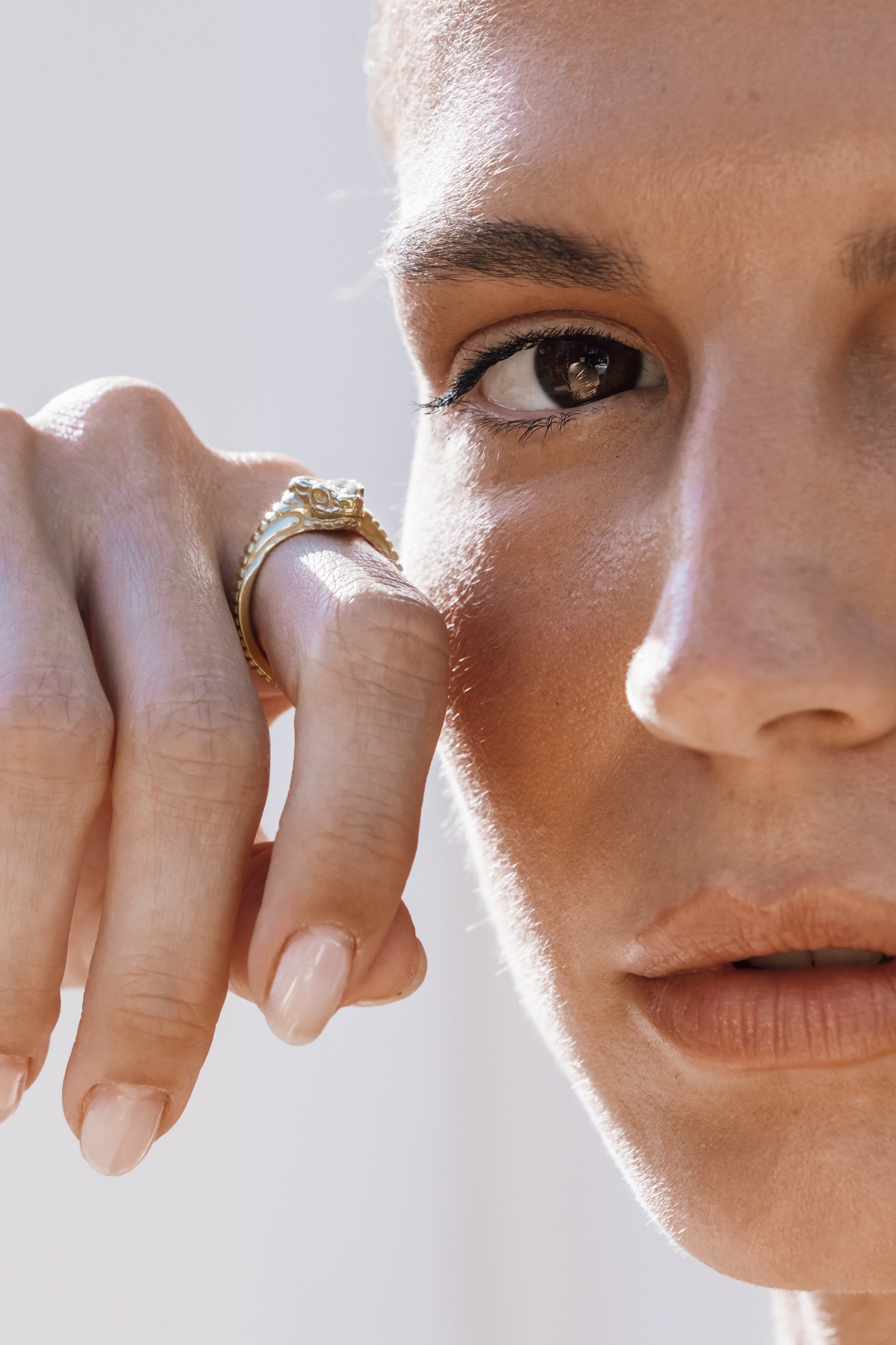 Close-up of a person wearing a gold snake ring on a neutral background