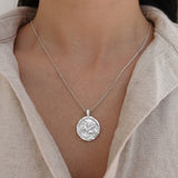 Silver necklace with a pegasus pendant worn by a person in a beige shirt.