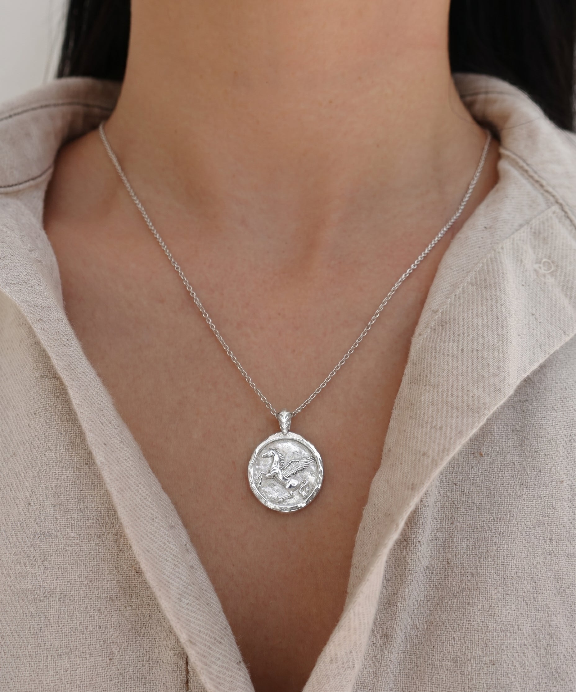 Silver necklace with a pegasus pendant worn by a person in a beige shirt.