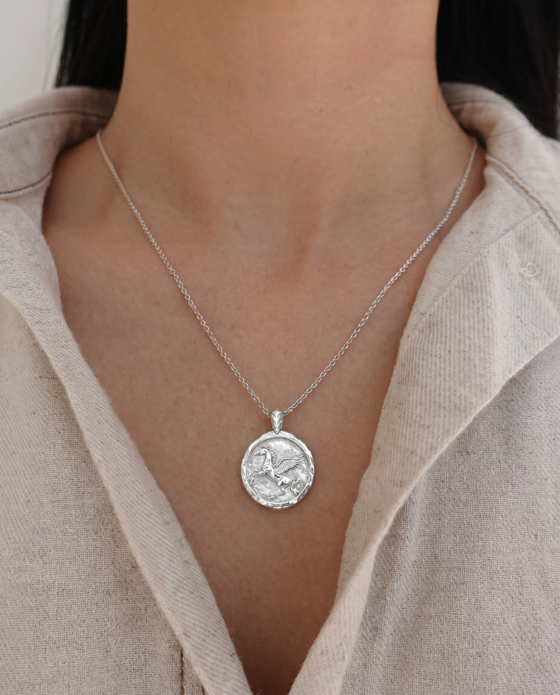 Silver necklace with a pegasus pendant worn by a person in a beige shirt.