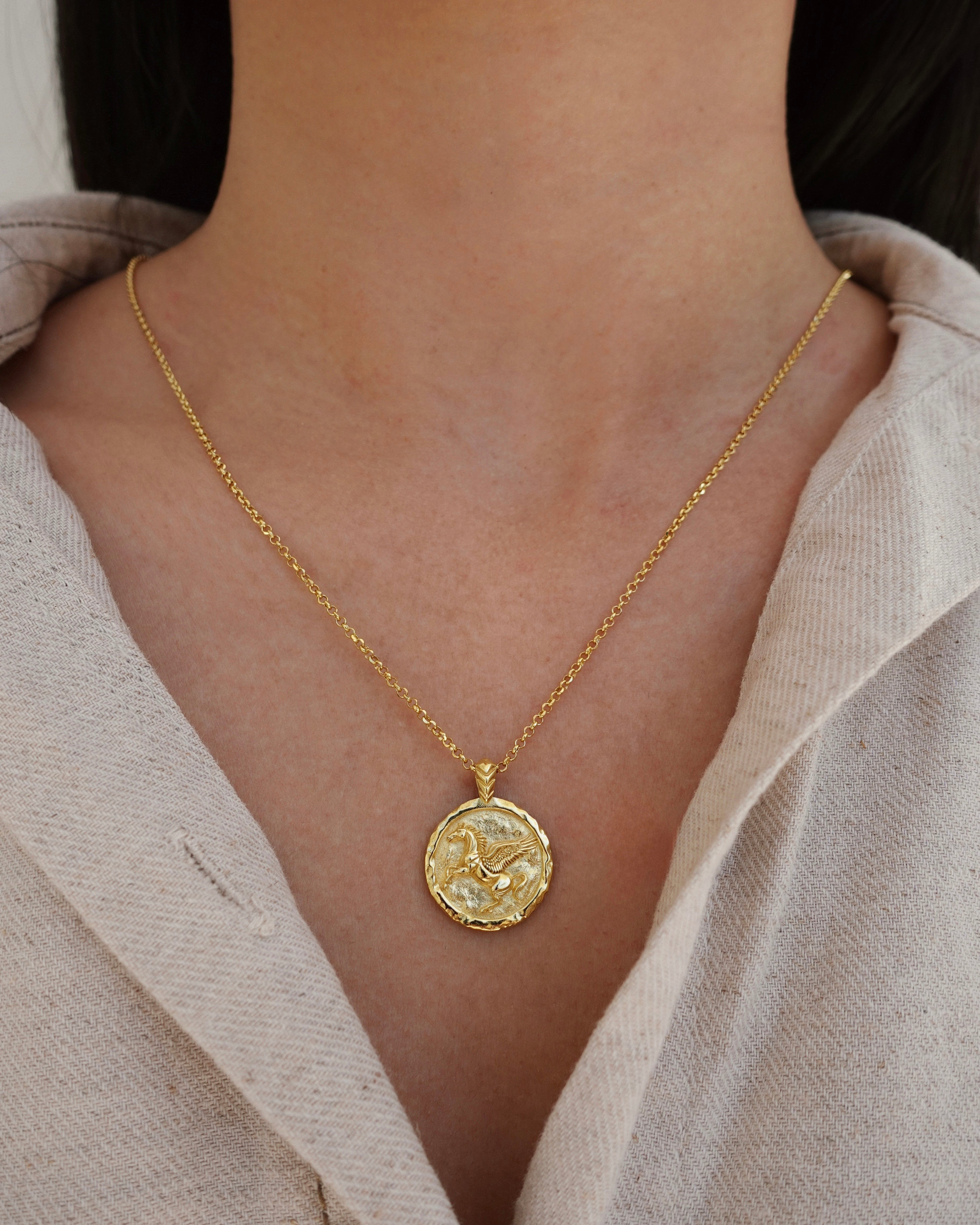 Gold necklace with a pendant worn by a person in a light-colored shirt.