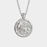 A silver pendant necklace featuring a circular, hammered-texture coin-style medallion with an embossed figure like ancient greek warrior holding a shield, suspended from a delicate silver chain against a light gray background.