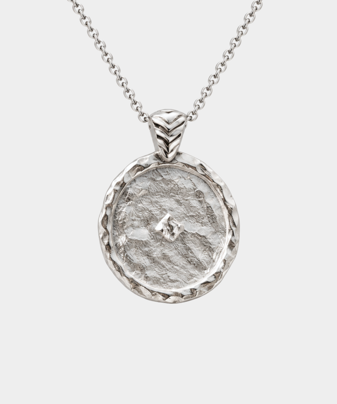 A silver pendant necklace featuring a hammered circular medallion with a textured organic surface and a small central star-like detail, suspended from a delicate silver chain against a light gray background.