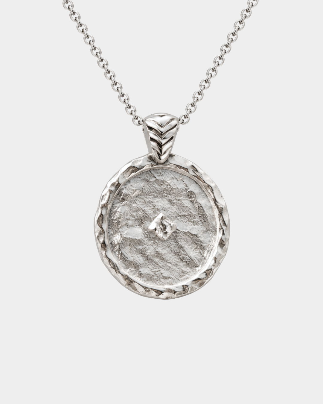 A silver pendant necklace featuring a hammered circular medallion with a textured organic surface and a small central star-like detail, suspended from a delicate silver chain against a light gray background.
