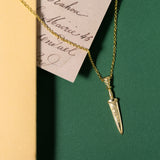 Gold necklace with a dagger pendant on a green surface
