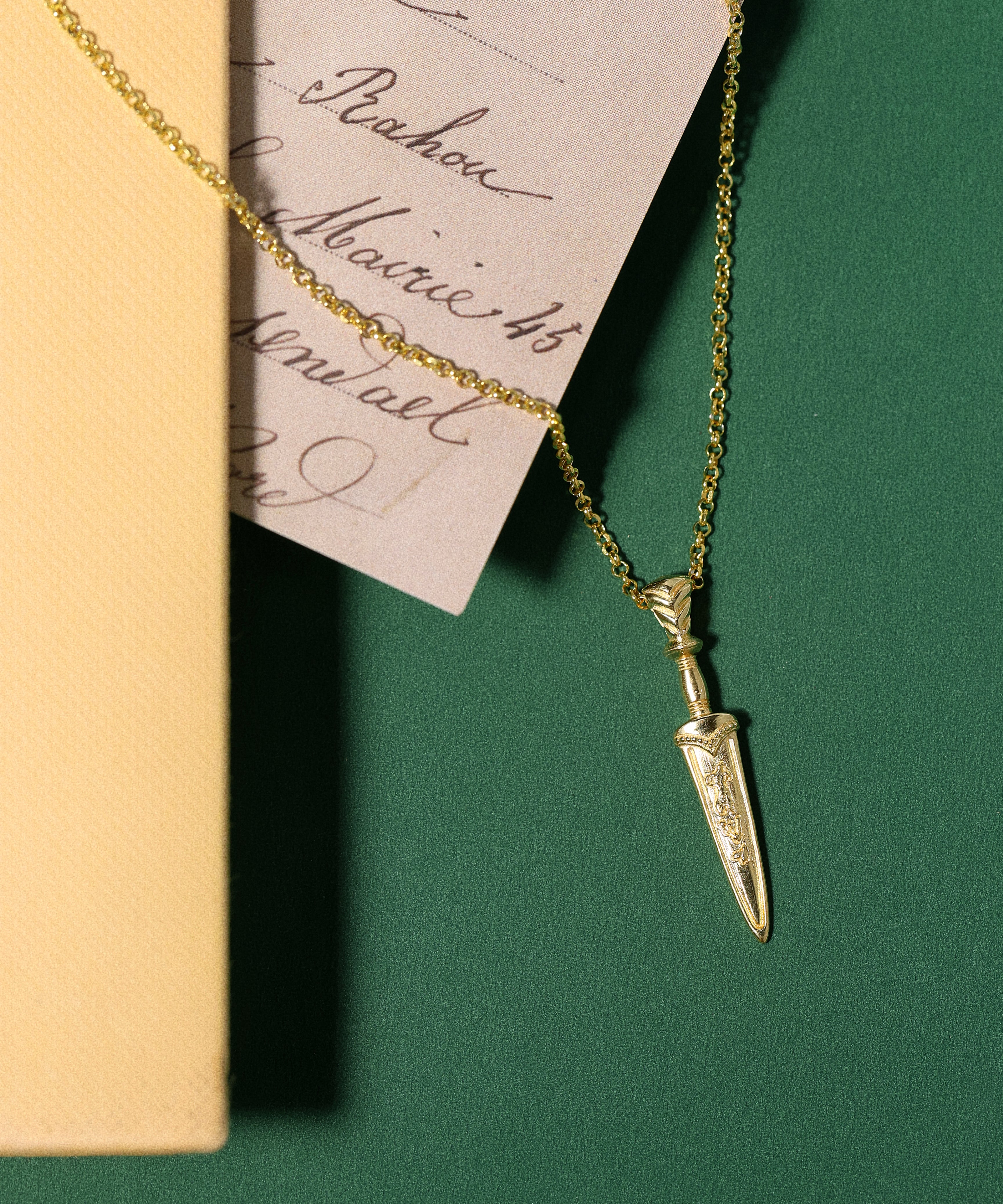 Gold necklace with a dagger pendant on a green surface